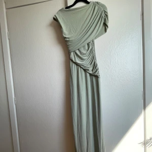 Ljusgrön långklänning från PrettyLittleThing - Supersnygg ljusgrön långklänning från PrettyLittleThing med draperad design och oneshoulder. Klänningen har en elegant omlottkänsla och är tillverkad i mjuk polyester som faller snyggt. Perfekt för dig som vill sticka ut med en unik siluett. Fick sminkfläck när jag prova se bild