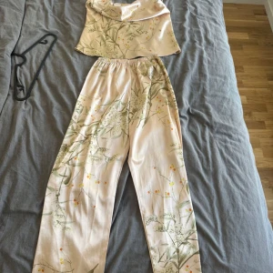 Pyjamas set i satin S - Snyggt pyjamas set i satin med blommigt mönster i grönt och gult. Byxorna har elastisk midja och rak passform, perfekta för en chill hemma kväll. Lätta och sköna med en lyxig känsla, passar perfekt till sommaren.