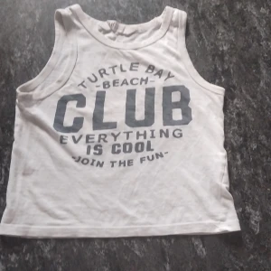 Vit linnetopp från H&M med tryck - Säljer en vit linnetopp från H&M i bomull med stort tryck på framsidan: 'Turtle Bay Beach Club Everything is cool Join the fun'. Klassisk ärmlös modell med rund halsringning, perfekt för varma dagar.