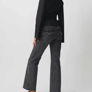 Grå bootcut jeans med dubbla knappar - Snygga grå jeans från gina med bootcut-ben och dubbla knappar i midjan. Jeansen har klassiska fem fickor, svarta sömmar och en cool tvättad finish. Perfekta för dig som gillar en avslappnad men trendig look.