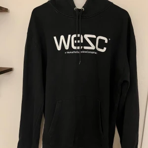 Svart WESC hoodie med tryck - Svart hoodie från WESC med stor vit logga framtill. Klassisk känguruficka, huva med snörning och lång ärm. Perfekt för dig som gillar streetwear och vill ha en enkel men snygg look. Mjuk bomullskänsla och relaxed fit.