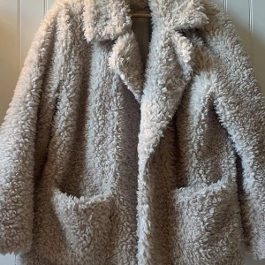 Beige teddyjacka med stora fickor - Supermjuk och fluffig teddyjacka från H&M i storlek L i beige med bred krage och två stora fickor fram🥰 Jackan har en oversized passform och är fodrad med slätt tyg för extra komfort. Perfekt för dig som vill ha en cozy och trendig look under kyliga dagar!💗