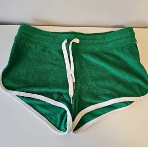 Gröna frottéshorts från H&M Basic - Sportiga gröna shorts från H&M Basic i mjuk frotté med vita kanter och snörning i midjan. Perfekta för sommardagar eller chill hemma. Materialet är en mix av polyester och bomull som känns skönt mot huden.