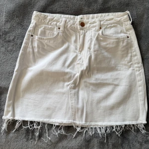 Ny vit jeanskjol med fransad kant H&M - •Aldrig använd. Storlek 38 •Vit jeanskjol från H&M med klassisk femficksdesign och fransad nederkant.  •Kjolen är kort och har en snygg, enkel look som passar perfekt till sneakers eller sandaler.  •Stängs med knapp och dragkedja framtill.  •Perfekt för en chill sommarstil.