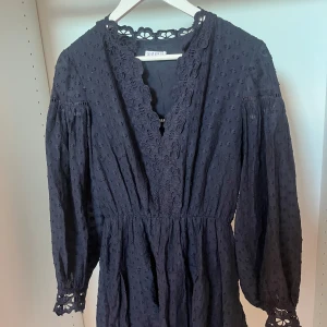 Mörkblå spetsklänning Claudie Pierlot - Supersöt mörkblå kortklänning från Claudie Pierlot med v-ringning, broderade spetsdetaljer vid hals och ärmslut samt långärmad design. Klänningen har markerad midja och ett diskret strukturmönster i tyget. 