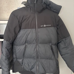 Svart pufferjacka från Sail Racing XS - Säljer en svart pufferjacka från Sail Racing i storlek XS. Jackan har hög krage, huva och två dragkedjeförsedda fickor. Den är vadderad och har en clean look med Sail Racing-logga på bröstet. Perfekt för kalla dagar när du vill hålla stilen. Smink som kommit på jackan däruppe kan försöka få bort det! Kvitto finns!