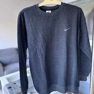 Mörkgrå sweatshirt  - En stilren mörkgrå sweatshirt med rund halsringning, ribbade muddar och är långärmad. Perfekt för en chill och sportig look. Mjukt och tjockt material. Oanvänd utan prislapp.