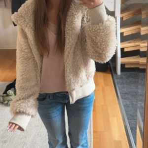  teddyjacka zara - Supermjuk och fluffig teddyjacka från Zara TRF i beige. Jackan har dragkedja framtill, ribbade muddar och krage. Perfekt för att hålla sig varm och snygg under kyliga dagar. Passar dig som gillar en avslappnad och trendig stil.