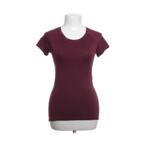 Vinröd träningströja - Säljer en vinröd, figurnära träningstopp med korta ärmar och rund hals. Enkel och stilren design som sitter snyggt på kroppen. Perfekt för dig som gillar en clean och sportig look.