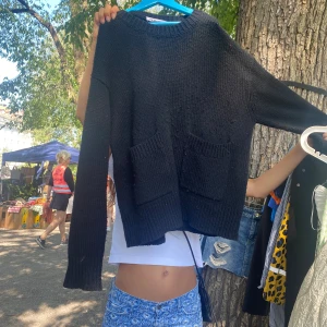 Svart stickad tröja med fickor - Svart stickad tröja med två stora fickor framtill och rund halsringning. Tröjan har lång ärm och en lite loose passform, perfekt för lager-på-lager-stil. Enkel och stilren design som funkar till det mesta.