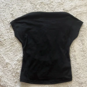 Svart croppad topp med kort ärm med öppen rygg - En svart croppad topp med korta ärmar och bred halsringning. Toppen har en enkel och stilren design, perfekt att matcha med jeans eller kjol. Materialet känns mjukt och stretchigt, vilket gör den bekväm att bära hela dagen.