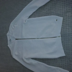 Vit ribbad kofta från Hampton Republic - Vit ribbad kofta från Hampton Republic i storlek S. Tröjan har en snygg guldfärgad dragkedja framtill och är tillverkad i ett mjukt, stickat material. Långärmad och med klassisk passform, perfekt för lager-på-lager-stil.❤️🌟