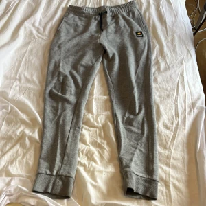 Grå mjukisbyxor från CLWR - Snygga grå mjukisbyxor från CLWR med svart snörning i midjan och ribbade muddar vid bensluten. Byxorna har en broderad logga på vänster ben och är tillverkade i mjukt bomullsmaterial. Perfekta för chill eller träning.