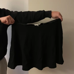 Svart kortkjol  - Enkel och stilren svart kortkjol med lätt utställd passform. Kjolen är gjord i mjuk bomull och har en klassisk look som är lätt att matcha med olika toppar. Perfekt för dig som gillar en basic men snygg vibe. Aldrig använd 