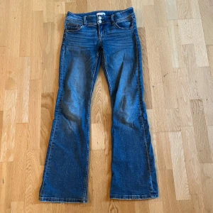 Blå bootcut jeans med fickdetaljer - Snygga blå jeans med bootcut passform och klassisk femficksdesign. Jeansen är lågmidjade. Har en liten slitning bak på ena byxbenet men något som verkligen inte syns. Storlek 158 från Gina tricot