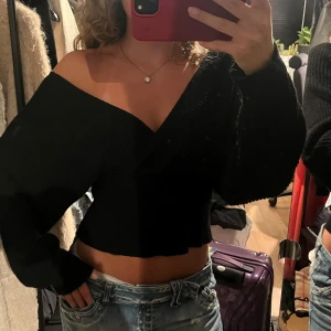 Svart croppad omlottstickad tröja - Svart stickad tröja med omlottmodell och croppad passform. Tröjan har djup v-ringning och långa ärmar