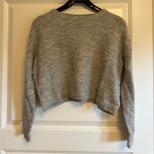 Grå höst vinter croppad stickad tröja H&M - Mysig grå stickad tröja med croppad passform och långa ärmar. Tröjan har en enkel, ribbad struktur och är perfekt för lager-på-lager-stil under kyliga dagar. Passar dig som gillar en avslappnad och trendig look.