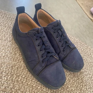 Navy blue Louboutin - Snygga mörkblå sneakers från Christian Louboutin med klassisk röd sula och diskret logga undertill. Skorna har rund tå, snörning och är tillverkade i canvas med detaljer i skinn. Perfekta för dig som vill ha en stilren men ändå lyxig look.