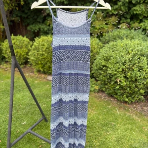 Blåmönstrad långklänning Casual Girls Wear - Långklänning med tunna axelband från Casual Girls Wear. Klänningen har ett blått och vitt geometriskt mönster i olika sektioner och är tillverkad i ett mjukt, lätt material. Perfekt för varma dagar när du vill ha något bekvämt och snyggt.