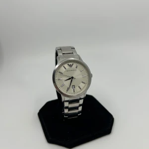 Emporio Armani silverfärgad klocka - Stilren klocka från Emporio Armani i silverfärgat rostfritt stål. Klassisk rund urtavla med datumvisning och diskreta indexmarkeringar. Länkar i metall ger en clean och modern look. Perfekt accessoar för dig som gillar minimalistisk design.