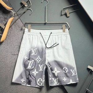 LV vita shorts med logga - Snygga vita shorts med svartvit LV-logga och mönster över hela framsidan. De har elastisk midja med svart snörning och är tillverkade i ett lätt material som passar perfekt till sommaren. Stilen är modern och streetinspirerad.