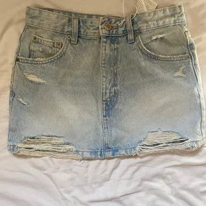 Ljusblå jeanskjol från Pull&Bear - Säljer en snygg ljusblå jeanskjol från Pull&Bear i storlek S. Kjolen har slitna detaljer, rå kant nertill och klassiska fem fickor. Helt ny, har aldrig använt