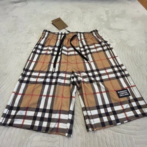  Burberry shorts  - Snygga shorts från Burberry med klassiskt rutigt mönster i beige, svart, vitt och rött. Modellen har elastisk midja med svart snörning och en patch med Burberry London England på benet. Perfekta för sommaren och ger en clean streetstyle-vibe.