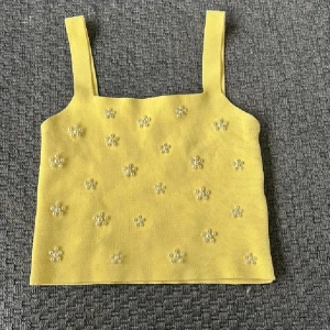 Gul pärlprydd linnetopp från Zara - Superfin gul linnetopp från Zara med breda axelband och dekorerad med små pärlor i blommönster över hela toppen. Perfekt för att liva upp din outfit med en färgklick och söta detaljer. Toppens material känns mjukt och har en lätt stickad känsla.