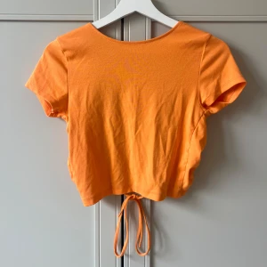 Croppad topp med snörning - Orange croppad topp i bomull med korta ärmar och öppen rygg. Toppen har snörning och knytning bak.
