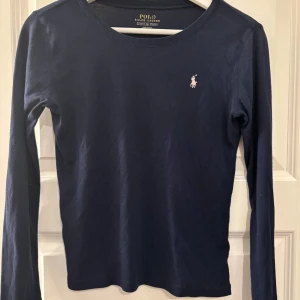 Marinblå långärmad tröja Polo Ralph Lauren - Snygg marinblå långärmad tröja från Polo Ralph Lauren i mjuk bomull. Klassisk passform med rund hals och logga i ljusrosa på bröstet. Barn/ ungdoms tröja. ( Endast köp via Plick) 