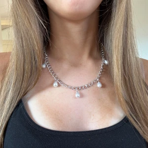Pärlhalsband Silver - Snyggt halsband i chunky silverfärgad kedja med fem droppformade pärlor som hänger längs kedjan. Ger en cool och trendig vibe till din outfit och passar perfekt om du vill sticka ut lite extra. Perfekt accessoar för att lyfta din look.