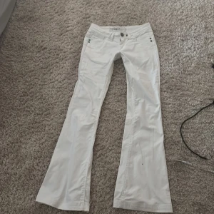 Vita bootcut jeans från Galstar - Snygga vita jeans från Galstar med bootcut-modell och låg midja. Byxorna har klassiska fem fickor, dekorativa nitar och broderade detaljer på bakfickorna. Perfekta för dig som vill ha en fräsch och stilren look. midjemåttet är 37 och innerbenslängden 82 cm