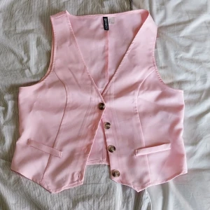 Ljusrosa väst från H&M Divided - Säljer en ljusrosa väst från H&M Divided i storlek S. Västen har v-ringning, tre knappar framtill och två fejkade fickor. Snygg figursydd passform och klassisk look.