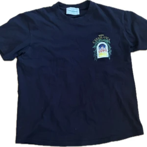 Svart t-shirt från Casablanca - Cool svart t-shirt från Casablanca med färgglatt tryck av en byggnad och gröna blad både fram och bak. Klassisk passform med rund hals och korta ärmar