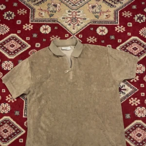 Beige pikétröja i frotté från Grunt - Säljer en beige pikétröja från Grunt i mjuk frotté. Tröjan har korta ärmar, klassisk krage och en half zip-dragkedja framtill. Perfekt för dig som gillar en chill och avslappnad stil med lite retrovibe.