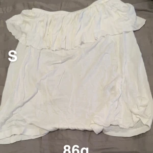 Vit offshoulder tubtopp med volang - Säljer en vit offshoulder tubtopp med bred volang upptill. Toppen är ärmlös och har en luftig, flowy passform som passar perfekt till sommaren. Enkel att styla med både jeans och kjol för en fräsch look.🌸 
