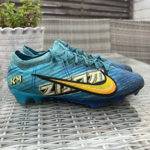 Nike Zoom Mercurial fotbollsskor blå/gul - Nike Zoom Mercurial fotbollsskor i blått med gula och svarta detaljer samt coolt grafiskt mönster på sidan. Skorna har snörning, stickad ovandel och mönstrad sula för grymt grepp på planen. Perfekta för dig som vill sticka ut på matchen.