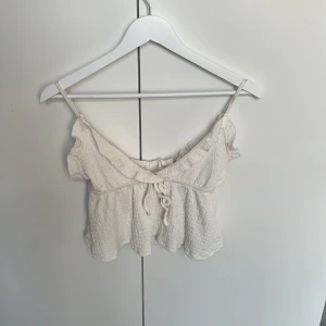 Vit volang topp från SHEIN - Supersöt vit linnetopp från SHEIN med smala axelband, volangdetaljer längs urringningen och knyt framtill. Toppen är croppad och har en lätt skrynklig struktur som ger en chill vibe. Perfekt för varma dagar och sommarhäng.