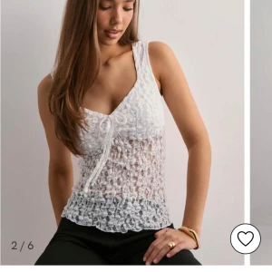 Vit spetsig linnetopp med knyt Nelly - Säljer en vit ärmlös linnetopp med spetsdetaljer och v-ringning. Toppen har en söt knytning framtill och är genombruten med blommigt mönster. Perfekt för sommarens alla tillfällen och ger en romantisk vibe.