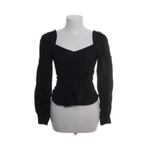 Svart blus med v-ringning och knyt - Snygg svart blus med v-ringad hals och långa ärmar. Toppen har markerad midja med knyt fram som ger en cool siluett. Perfekt för dig som gillar stilrena och trendiga plagg med det lilla extra.