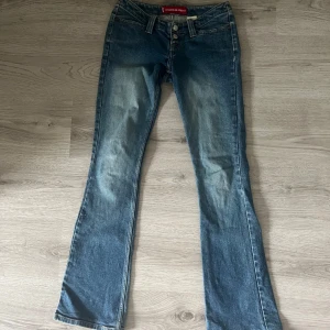 Levi's Too Superlow Stretch bootcut jeans - Snygga blå Levi's Too Superlow Stretch jeans med låg midja och bootcut-ben. Jeansen har klassisk femficksdesign, dubbla silverknappar och slitningar framtill för en cool vintagekänsla. Perfekta för dig som gillar 00-talsstil och vill ha en bekväm stretchig passform. Säljs inte längre.
