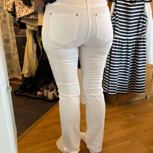 Vita bootcut jeans från Time, stl 42 - Snygga vita jeans från Time i storlek 42. Modellen har klassiska bakfickor med dekorativa sömmar och bootcut-ben som ger en schysst siluett. Jeansen är tillverkade i bomull och har en metallknapp med blommönster framtill.