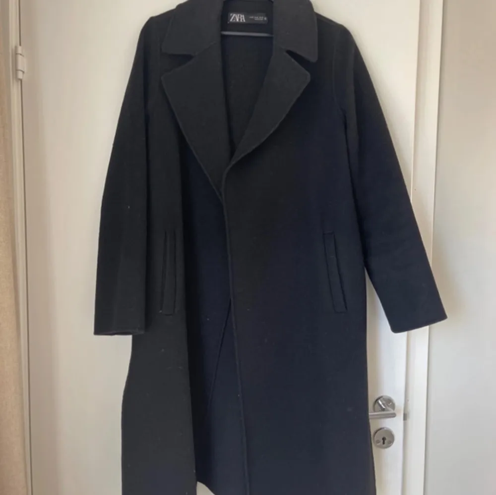 Elegant svart kappa från Zara med klassisk design. Den har långa ärmar och ett bälte i midjan för en stilren look. Perfekt för kyligare dagar.. Takit.