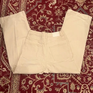 Beige byxor från Weekday - Säljer ett par stilrena beige byxor från Weekday. De har en klassisk design med raka ben och femficksmodell. Perfekta för en avslappnad men ändå snygg look.