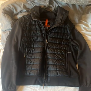 Svart jacka från parajumper - Snygg svart jacka från parajumpers  med quiltad design och dragkedja framtill. Jackan har en huva och praktiska fickor med dragkedjor. Vill få bort den då jag ej använder den längre, storleken är lx men skulle klassa den som en M/L då storleken inte sägs vad den är. Så som ni ser på bilden så är den inte jätte stor egentligen 