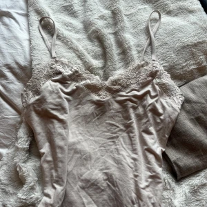 Beige linnetopp från Intimissimi - Säljer en elegant beige linnetopp från Intimissimi med spetsdetaljer vid halsringningen. Toppen har smala axelband och är perfekt för en stilren look. Passar bra till både jeans och kjol.