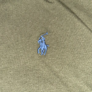 Olivgrön t-shirt från Polo Ralph Lauren - Säljer en stilren olivgrön t-shirt från Polo Ralph Lauren med det klassiska broderade logotypen i blått på bröstet. T-shirten är kortärmad och tillverkad i mjuk bomull, perfekt för en avslappnad look. Passar perfekt till jeans eller shorts!