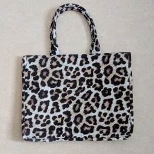 Leopardmönstrad handväska - Snygg leopardmönstrad handväska med två handtag. Väskan har ett dragkedjeförsett innerfack för säker förvaring av småsaker. Perfekt för att ge en djärv touch till din outfit. Väska från HM. 