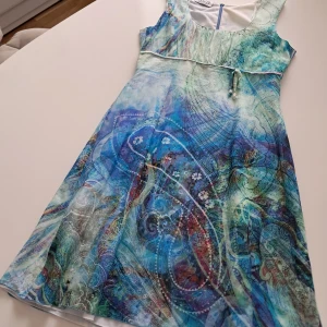 Mönstrad klänning från Tuzzi - Säljer en färgglad klänning från Tuzzi med ett unikt mönster i blå och gröna toner. Klänningen är ärmlös och har en lätt A-linjeform. Materialet består av bomull och siden, vilket ger en lyxig känsla. Perfekt för sommarens varma dagar!