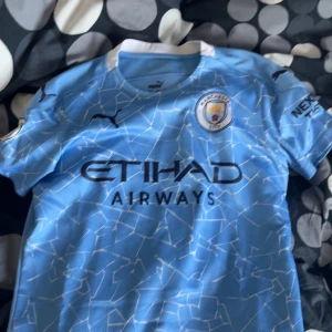 Ljusblå Manchester City fotbollströja - Säljer en ljusblå Manchester City fotbollströja från Puma med ett unikt vitt mönster. Tröjan har korta ärmar och klubbens emblem på bröstet. Namnet 'G. Jesus' och nummer 9 är tryckt på baksidan.